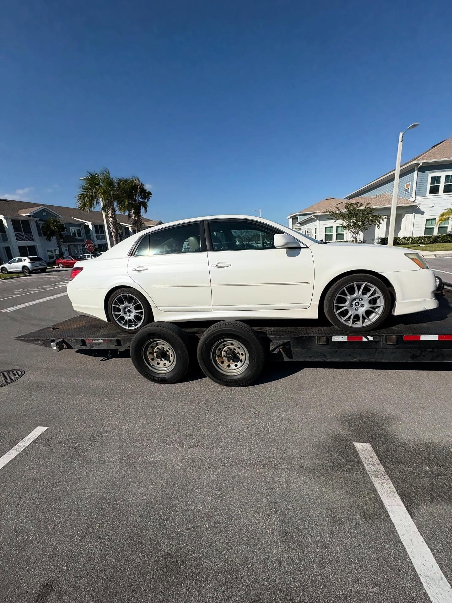 White sedan transported on a Hook & Book flatbed in Port St. Lucie